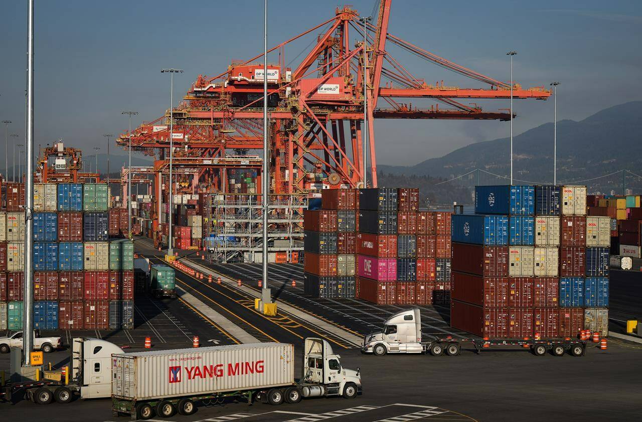 A truck carries a cargo container at the Port of Vancouver Centerm container terminal as others are stacked under gantry cranes in Vancouver on Friday, October 14, 2022. THE CANADIAN PRESS/Darryl Dyck