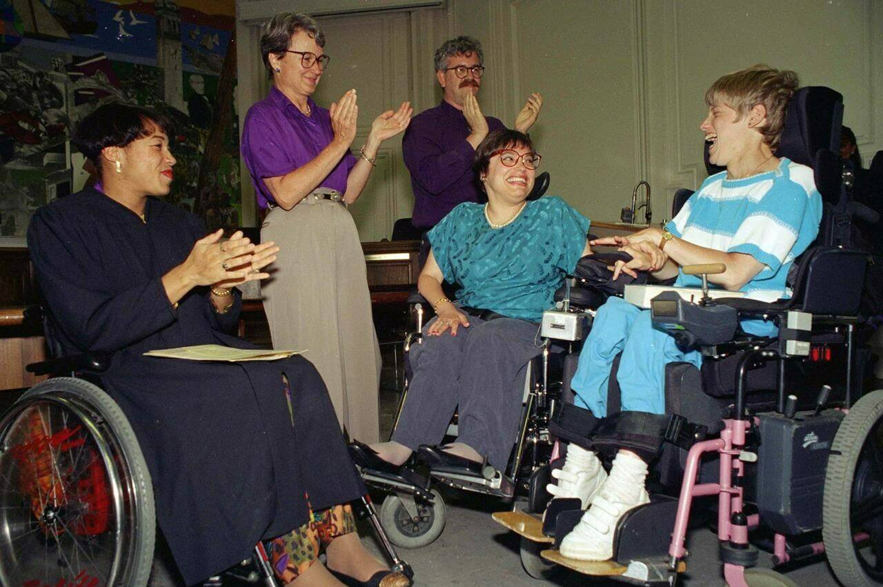 FILE - Judy Heumann, center, is applauded during her swearing-in as U.S. Assistant Secretary for Special Education and Rehabilitative Service by Judge Gail Bereola, left, in Berkeley, Calif., on Tuesday, June 29, 1993. Standing at left is Berkeley Mayor Loni Hancock with sign language interpreter Joseph Quinn, and Julie Weissman, right, in attendance with a large audience. Heumann, a renowned disability rights activist who helped secure legislation protecting the rights of disabled people, has died at age 75. The news of her passing on Saturday, March 4, 2023, in Washington, was shared on her website and social media accounts. (AP Photo/Susan Ragan, File)