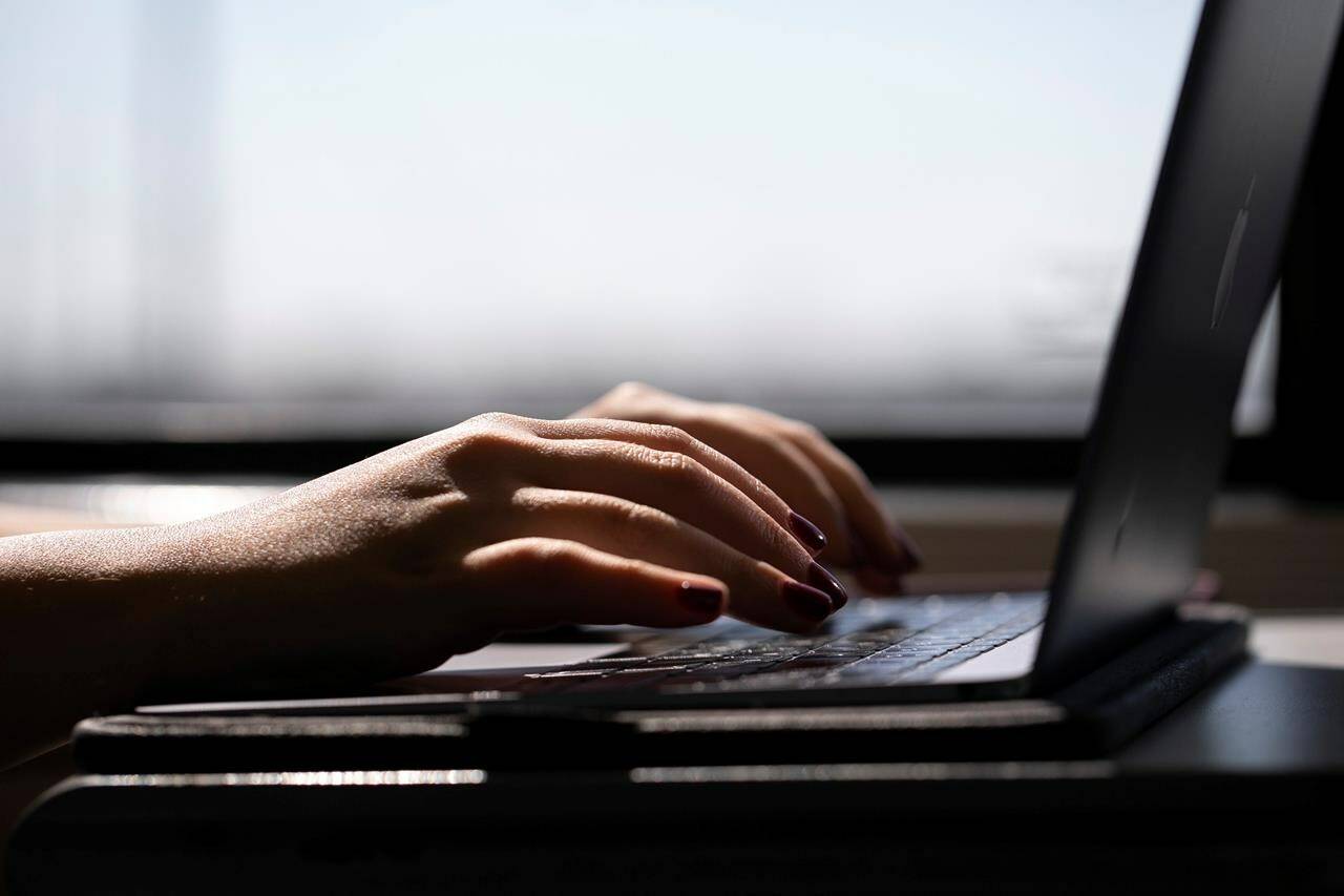 A woman types on a laptop on a train in New Jersey on May 18, 2021. A panicked 14-year-old from British Columbia and his family paid $1,500 to a company that claimed it would recover intimate images that were being used to extort him. It didn’t. THE CANADIAN PRESS/AP, Jenny Kane
