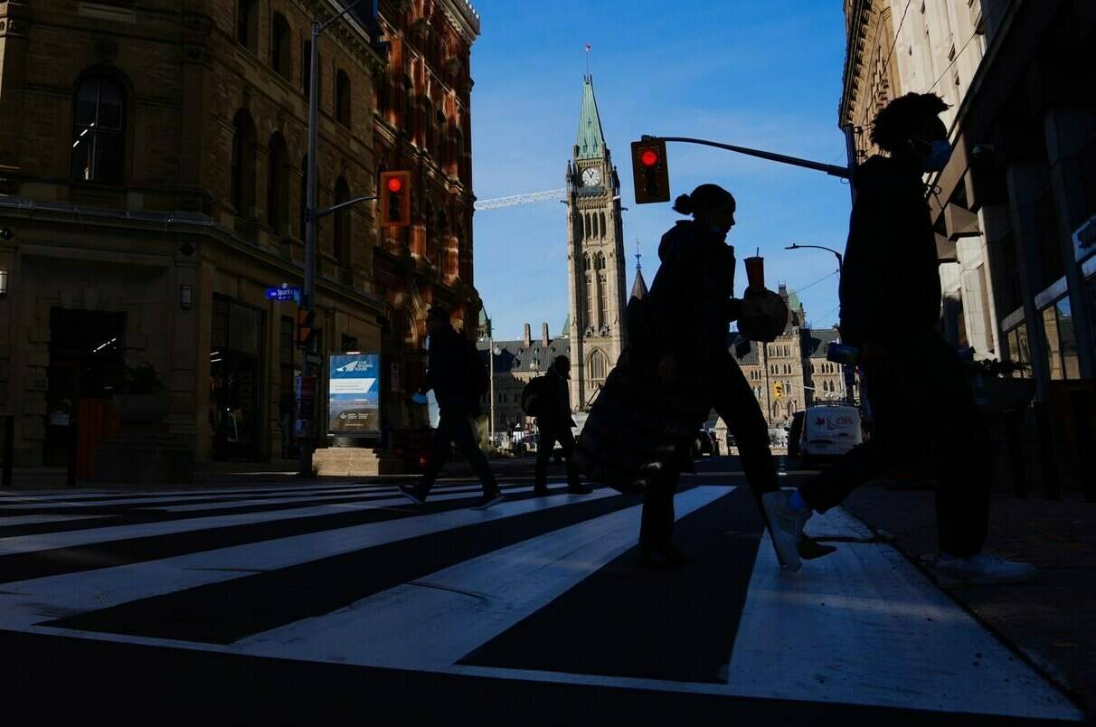 The Canada Flag flies on the Peace Tower of Parliament Hill as pedestrians make their way along Sparks Street Mall in Ottawa on Tuesday, Nov. 9, 2021. Federal public servants are expected to be back in office by the end of the month. THE CANADIAN PRESS/Sean Kilpatrick